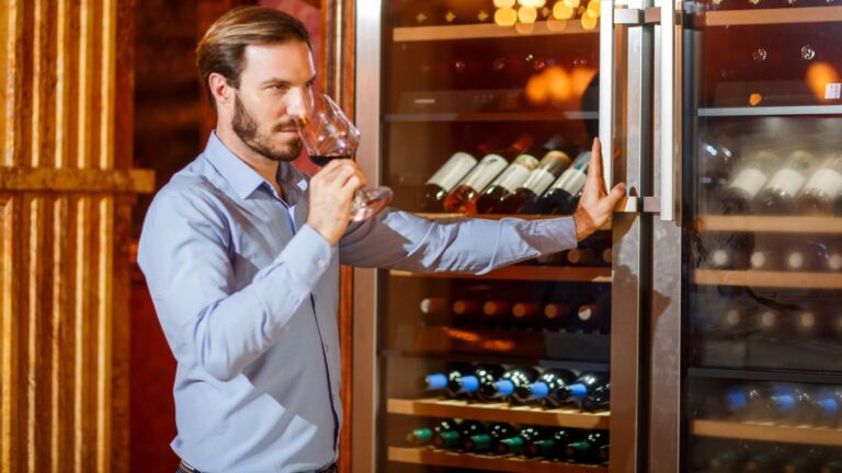 A sommelier tastes wine in front of a wine cooler